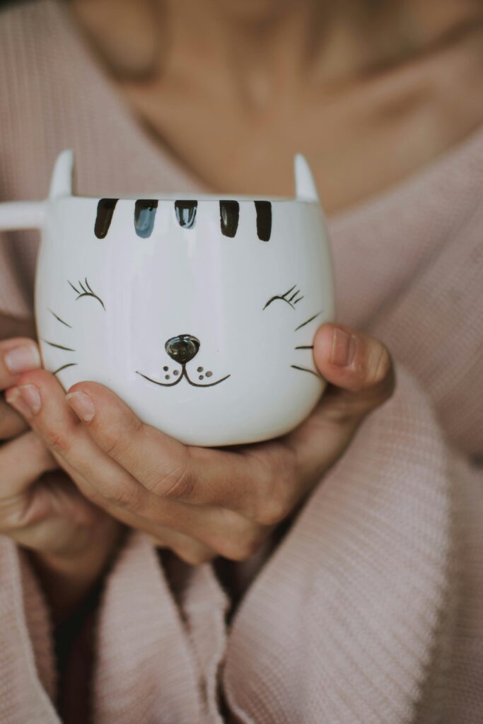 A woman holds a ceramic mug with a cute cat face design, perfect for cozy indoors setups.