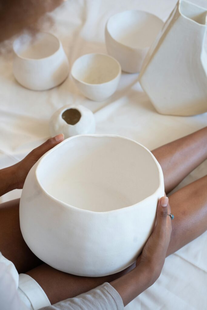 High angle of crop African American artisan sitting on floor with creative pottery in bright studio
